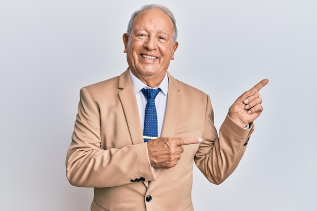 Senior caucasian man wearing business suit smiling and looking at the camera pointing with two hands and fingers to the side