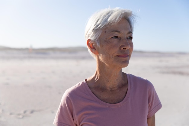 Senior Caucasian woman enjoying time at the beach on a sunny day, smiling with blue sky in the background