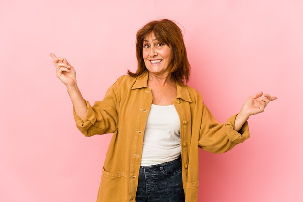 Senior caucasian woman isolated pointing to different copy spaces, choosing one of them, showing with finger.