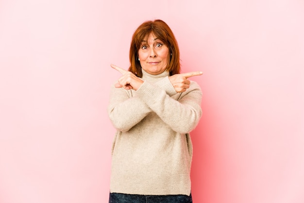 Senior caucasian woman isolated points sideways, is trying to choose between two options.