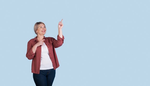 Senior caucasian woman with blonde hair pointing to the blue  free space near her with index finger