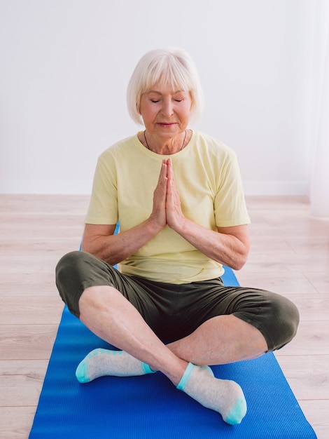 senior cheerful peaceful woman doing yoga indoor Namaste hands Anti age sport yoga concept