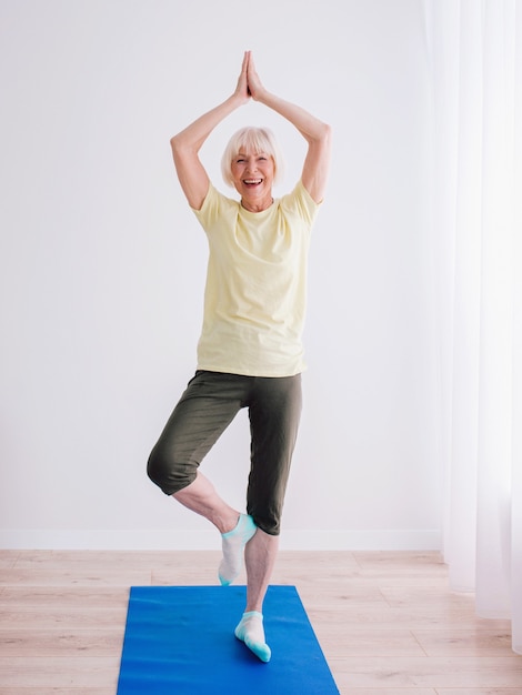 senior cheerful peaceful woman doing yoga indoor Namaste hands Anti age sport yoga concept