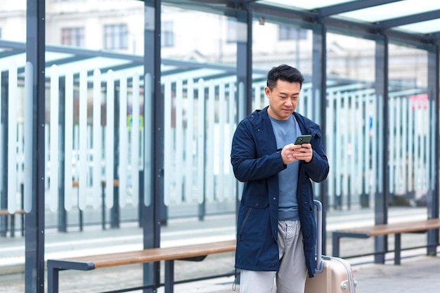 Senior chinese tourist uses mobile phone app to book accommodation and call taxi man near airport with suitcase