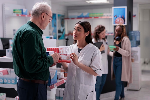 Senior client holding cardiology pills package asking for pharmacist medical advice during medication shopping in drugstore. Helpful druggist selling medicinal supplements. Health care service