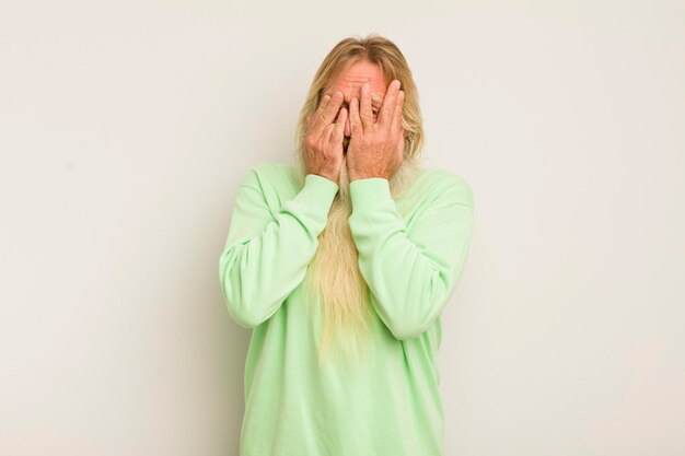 Senior cool bearded man covering face with hands peeking\
between fingers with surprised expression and looking to the\
side