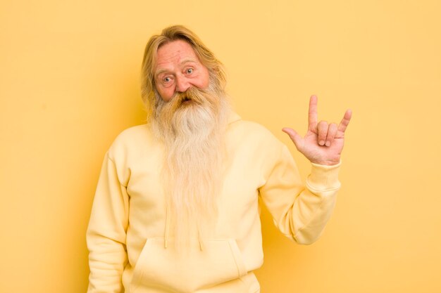 Senior cool bearded man feeling happy fun confident positive and rebellious making rock or heavy metal sign with hand