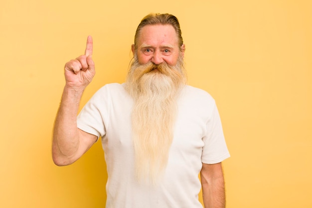 Photo senior cool bearded man smiling cheerfully and happily pointing upwards with one hand to copy space