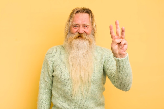 Senior cool bearded man smiling and looking friendly showing number three or third with hand forward counting down