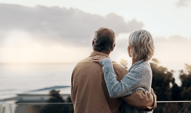 Senior couple back and hug with balcony for love embrace or outdoor holiday together at home Mature man or woman with view of nature in relax or romance for vacation or bonding on terrace at house