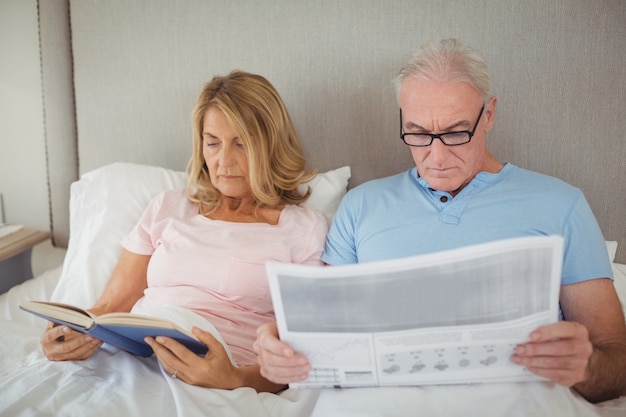 Senior couple on bed reading newspaper and book