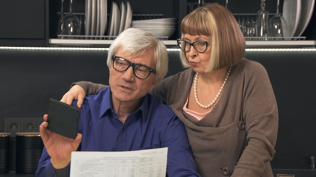 Senior couple calculate their bills on kitchen