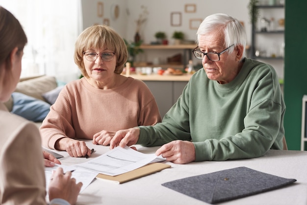 自宅で打ち合わせをしているコンサルタントと財務書類について相談する年配のカップル