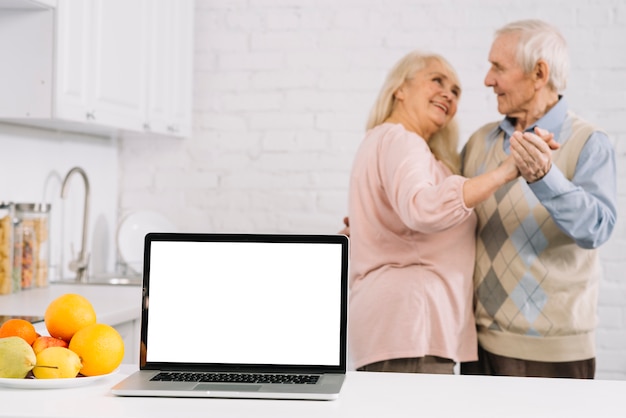 Пожилая пара танцует за ноутбуком на кухне