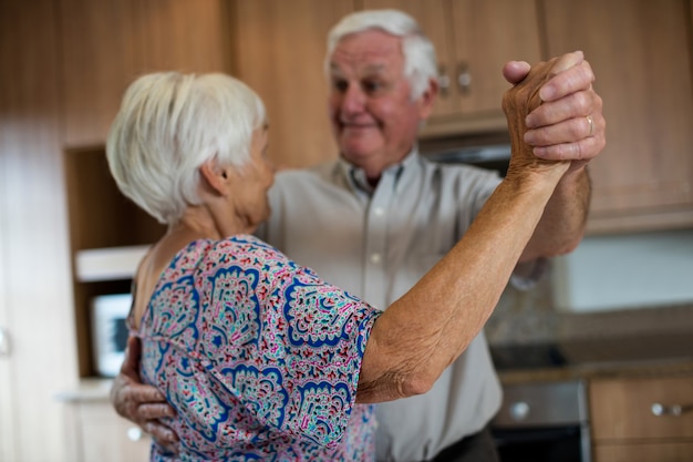自宅のキッチンで一緒に踊る年配のカップル