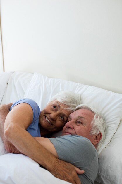 自宅の寝室で抱き合って抱き合う老夫婦
