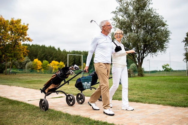 Coppia senior che si gode il tempo libero in pensione giocando a golf e camminando verso il campo pratica