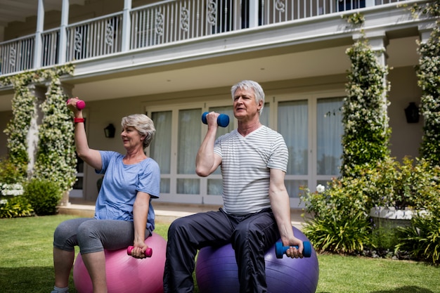 Пожилые супружеские пары, осуществляющие с гантелями на фитнес-мяч
