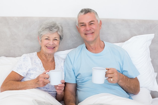 Senior couple holding coffee cups in bed