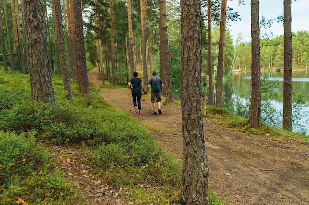 senior couple holding hands walking in forest along lakeside