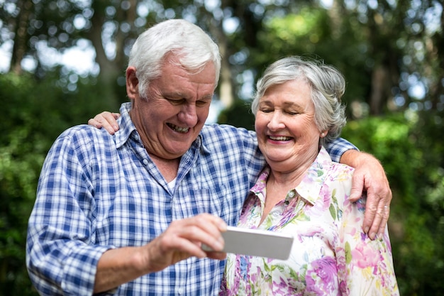 Пожилые супружеские пары, держа смартфон на заднем дворе