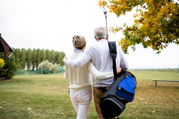 Senior couple holding together and enjoying recreational time in retirement by playing golf.