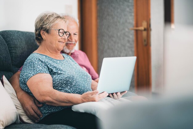 Coppia senior a casa che si rilassa utilizzando il laptop insieme nuovo stile di vita moderno per pensionati maturi uomo e donna con computer e connessione internet seduti sul divano nel tempo libero al coperto