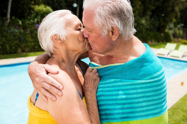 Пожилая пара целует друг друга у бассейна в солнечный день
