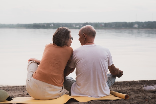 Senior couple in love sitting on beach an summer sunset tim