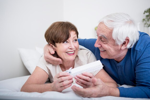 Senior couple lying in bed, man giving present to woman