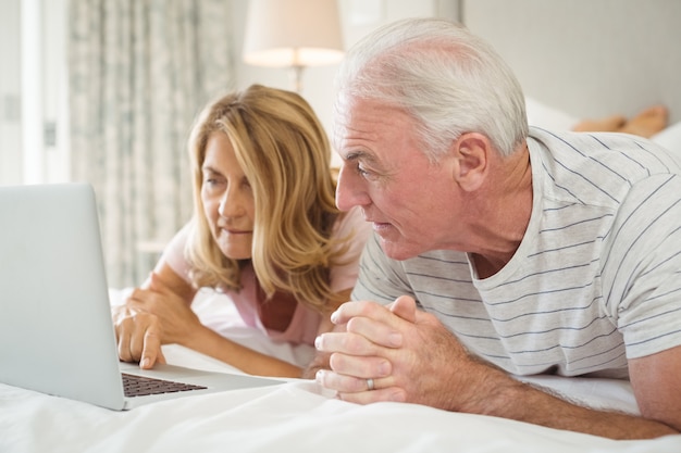 Coppie senior che si trovano sul letto e che per mezzo del computer portatile