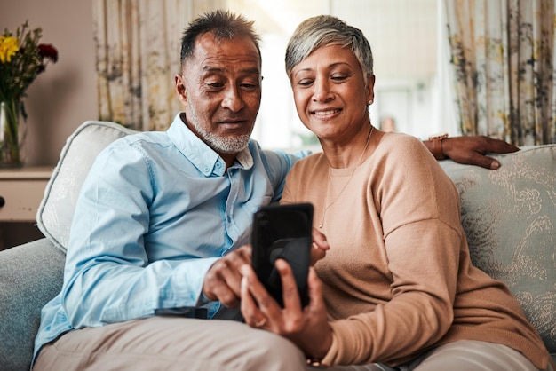 Пожилая пара звонит и читает на домашнем диване с интернет-сетью и любовью Зрелые мужчина и женщина отдыхают вместе на диване со смартфоном для потоковой передачи и онлайн-новостей или социальных сетей