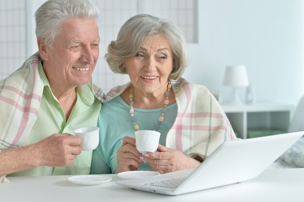 Портрет старшей пары с ноутбуком и чаем дома