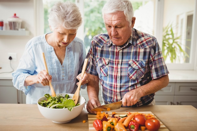 senior couple preparing salad in kitchen