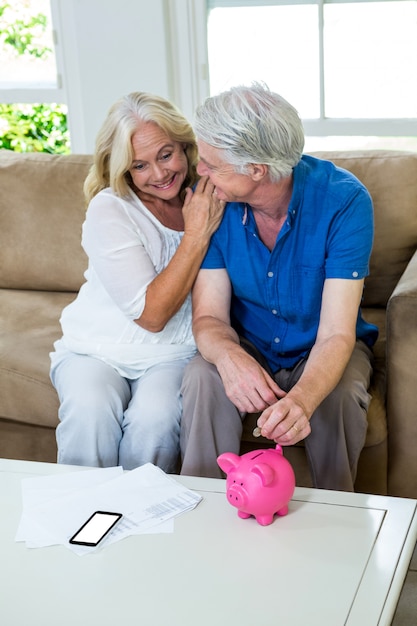 Senior couple putting coin in piggy bank while sitting at home