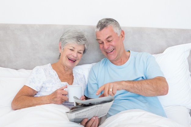 Senior couple reading newspaper in bed