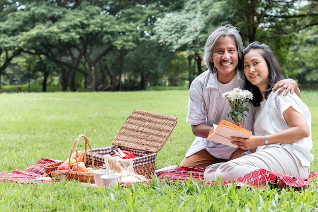 Senior couple relaxing and picnic at park.Wife give flower to my husband.