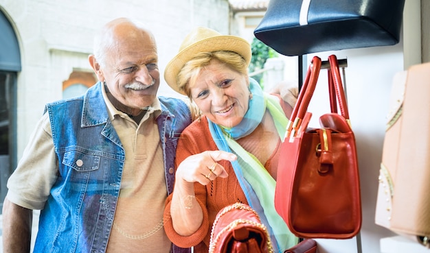 Senior couple shopping at fashion bag store with wife pointing showcase to husband