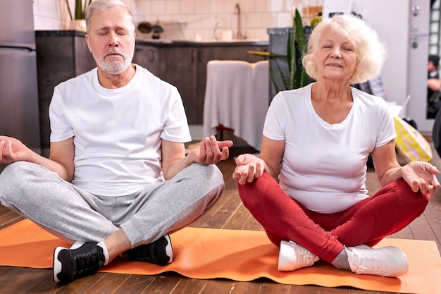 Senior couple sit on the floor meditating in lotus pose, engaged in yoga, keep calm with eyes closed