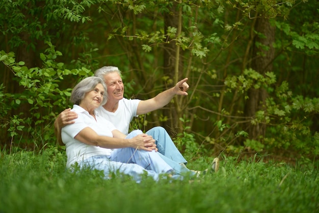 Senior couple sit on a ground in summer forest