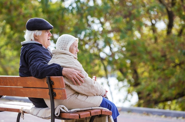 Senior couple sitting on bench in park and enjoying beautiful autumn day