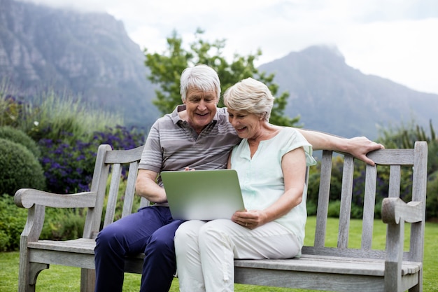 Photo senior couple sitting on bench and using laptop