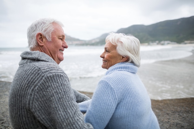 Coppie senior che si siedono sulla roccia alla spiaggia