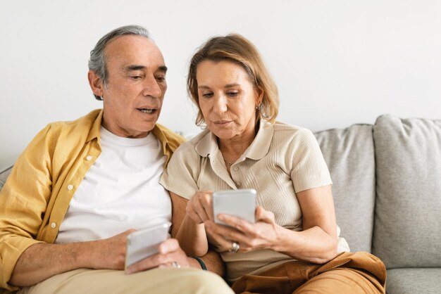 Senior couple sitting on sofa and using smartphone trying to understand mobile application