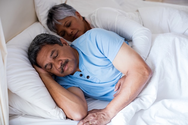 Senior couple sleeping together on bed in bedroom