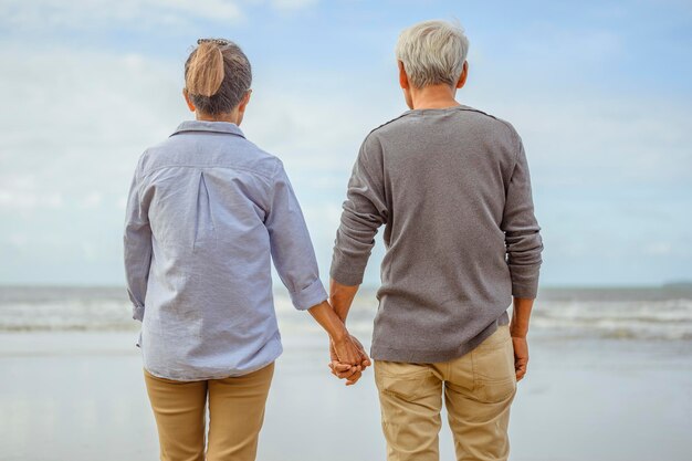 日の出で手をつないでビーチに立っている年配のカップルは、引退の概念で生命保険を計画します。