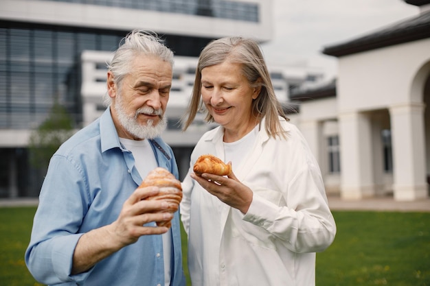 Senior couple standing on a grass in summer and holding two croissants