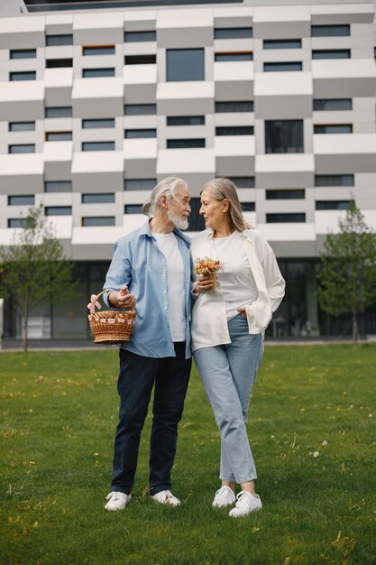 Senior couple standing on a grass in summer with straw basket and flowers