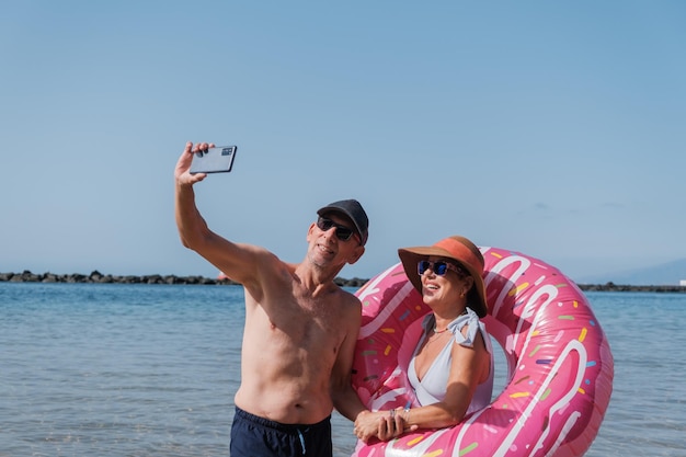 インフレータブルマットを使ってビーチで自撮りするシニアカップルコンセプトライフスタイル退職ビーチ