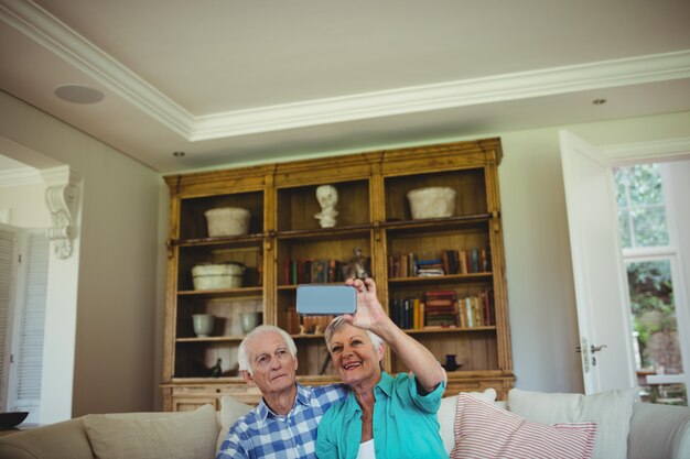 Photo senior couple taking a selfie on mobile phone in living room